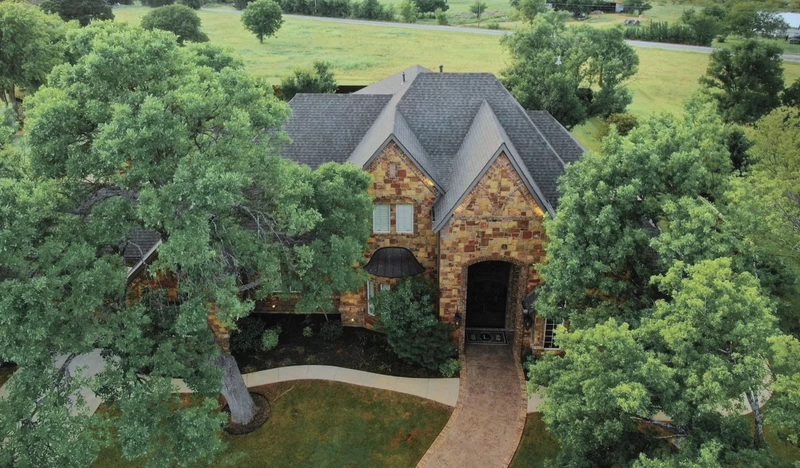 A stone two-story house outside Wichita Falls from the air, its gray shingle roof by Mataska