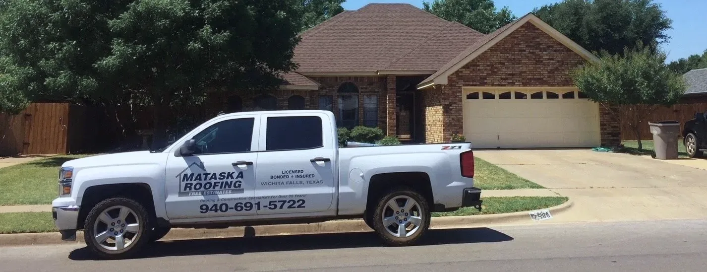 A Mataska Roofing pickup, phone number on the door, parked outside a brick house in Wichita Falls
